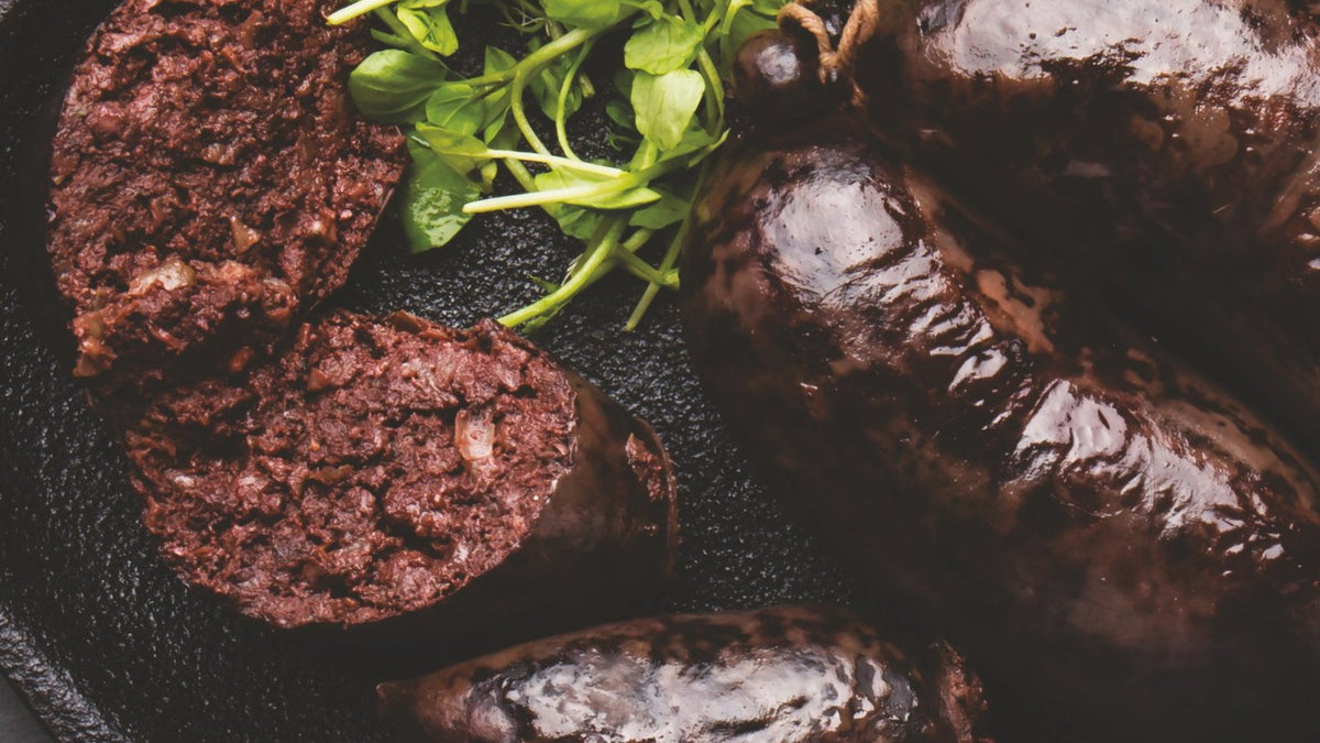 Belarusian blood sausage, sliced, with fresh greens on a dark pan, a photograph from The Belarusian Cookbook